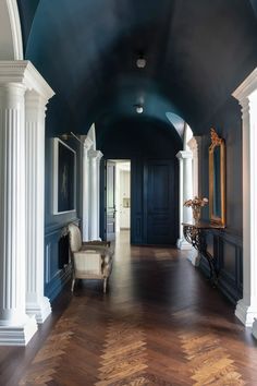 an empty hallway with blue walls and white columns on either side, leading to another room