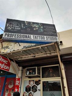 a tattoo studio sign hanging from the side of a building next to a store front