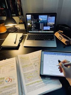 a person sitting at a desk with an open book and laptop computer on top of it