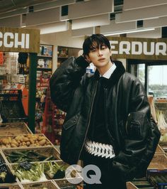 a young man in a black jacket standing next to produce at a grocery store with his hands on his head