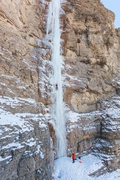 two people are climbing up the side of a mountain with a waterfall in the background