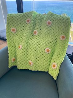 a green crocheted blanket sitting on top of a chair next to a window