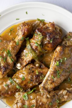 a white plate topped with meat covered in gravy and garnished with parsley