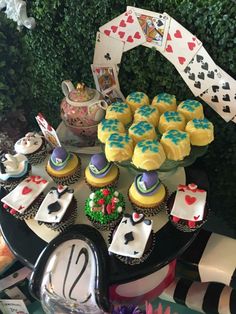 a table topped with lots of cupcakes covered in icing and playing cards