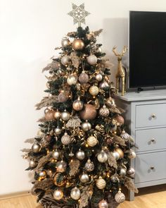 a decorated christmas tree with gold and silver ornaments in front of a flat screen tv