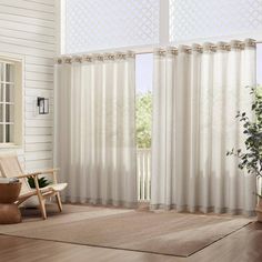 a living room with white curtains and a chair in front of the window that has a potted plant next to it