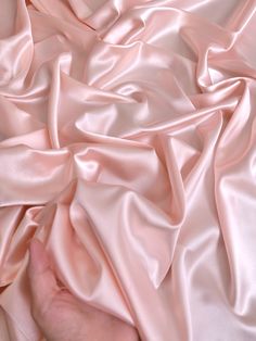 a person is holding their hand over a pink satin material that has been folded up