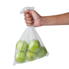 a person's hand holding a plastic bag full of green apples on a white background