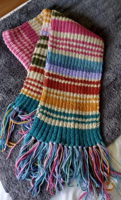 a multicolored scarf laying on top of a bed next to a gray blanket