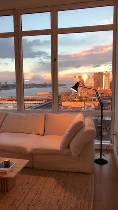 a living room filled with furniture and large windows overlooking the cityscape at sunset