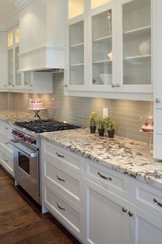 a kitchen with white cabinets and marble counter tops