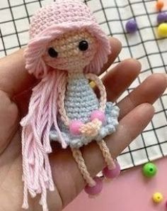 a hand holding a tiny crocheted doll in it's left hand with beads all around