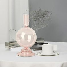 a pink vase sitting on top of a table next to a cup and saucer