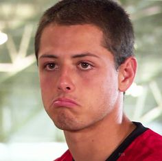 a close up of a person wearing a red shirt and looking at the camera with a serious look on his face