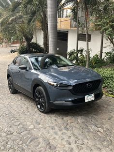 a grey mazda cx - 30 parked in front of a building with palm trees