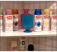 several different types of spray paint are on the shelf next to each other in front of white tiled walls