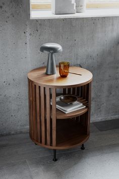 a round wooden table with a magazine rack on it and a glass in the middle