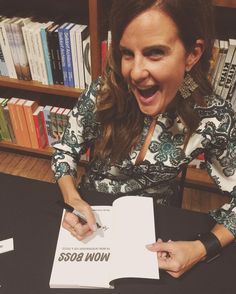 a woman sitting at a table with a book in front of her and making a funny face