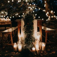 an outdoor setting with candles and greenery on the ground, surrounded by wooden chairs