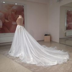 a white wedding dress on display in a room with pink walls and large floral paintings