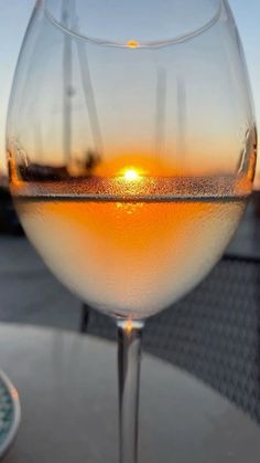 a wine glass sitting on top of a table with the sun setting in the background