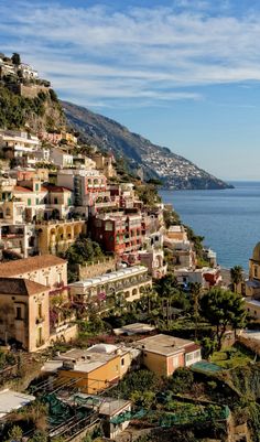 an aerial view of some buildings on the side of a hill by the ocean with mountains in the background