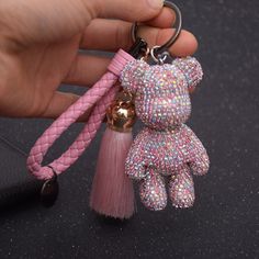 a hand holding a pink teddy bear keychain with a tassel on it