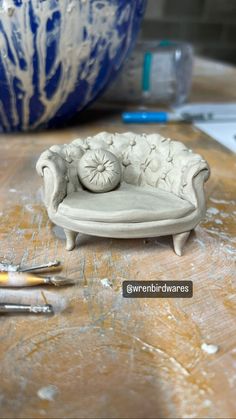 a small white couch sitting on top of a wooden table next to scissors and paint