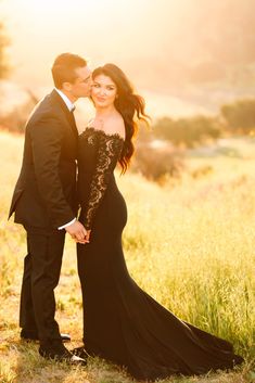 a man and woman in formal wear posing for a photo on the field at sunset