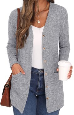 a woman wearing a gray cardigan sweater and jeans holding a coffee cup in her hand