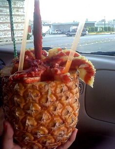 a person holding up a pineapple drink in their hand with sticks sticking out of it