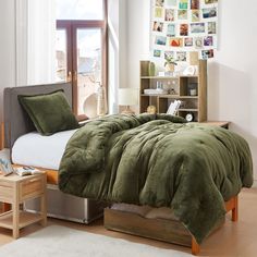 a bed with green comforter and pillows next to a window