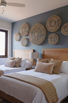 two beds in a room with wicker decorations on the wall above them and windows