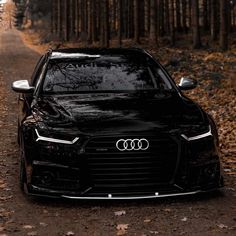 a black car parked on the side of a dirt road in front of some trees