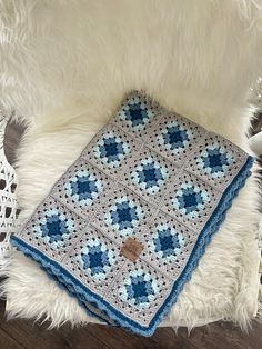 a blue and white crocheted blanket sitting on top of a furry rug in the middle of a room