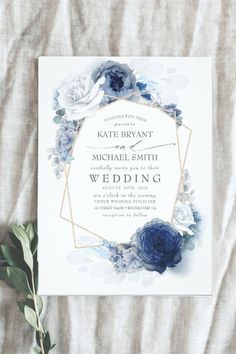 an elegant wedding card with blue flowers and greenery on the front, in gold frame