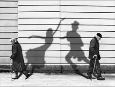 two people are walking down the street with their shadows on the wall and one is holding a cane