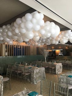 white balloons hang from the ceiling above tables and chairs in a banquet hall decorated with silver tablecloths