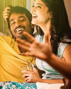 a man and woman sitting on top of a bed next to each other with their hands in the air