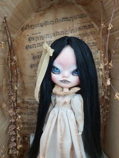 a doll with long black hair and blue eyes wearing a white dress in front of an old book