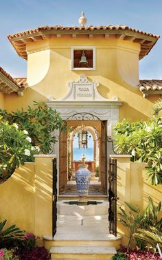 the front entrance to a yellow house with an archway and bell on it's side