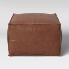 a brown leather cube ottoman with four square sections on the top and bottom, sitting in front of a white background