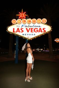 a woman standing in front of the welcome to fabulous las vegas sign at night time