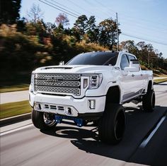 a white truck driving down the road with big tires on it's front wheels