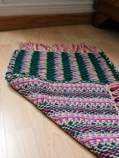 a cat laying on the floor next to a rug with multicolored stripes and fringes