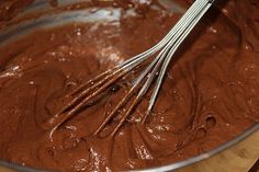 a bowl filled with chocolate and whisk on top of a wooden table