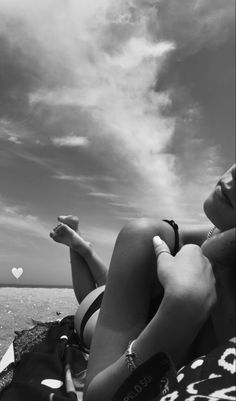 a woman laying on top of a beach next to the ocean under a cloudy sky