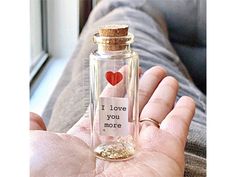 a person holding a small bottle with a message in it that says i love you more