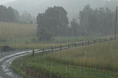 a car driving down a rain soaked road in the middle of an open grassy field