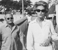 an old black and white photo of two people walking down the street with sunglasses on